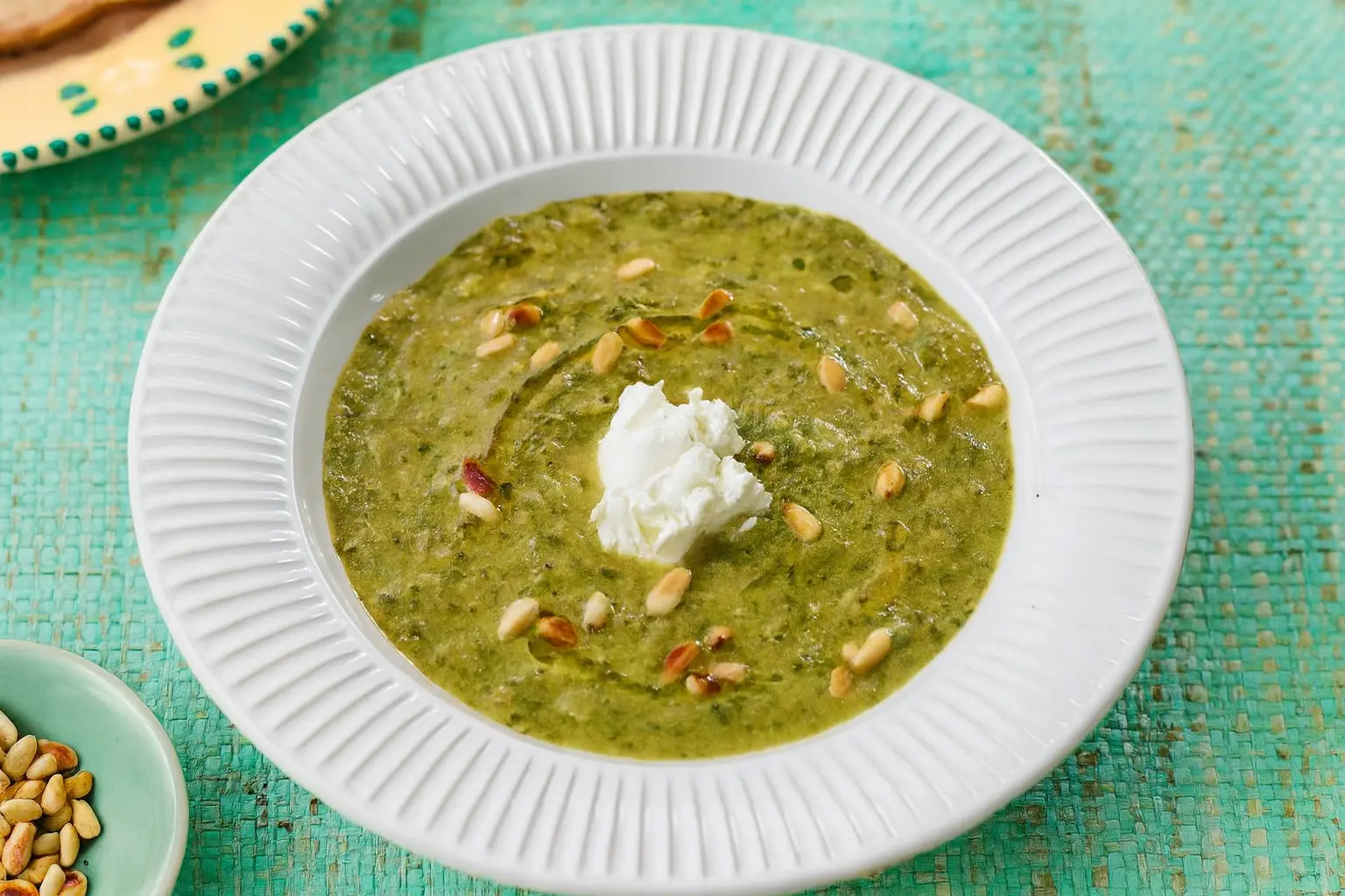 Bowl of roasted leek, celery and spinach soup topped with mascarpone, with pine nuts for garnish