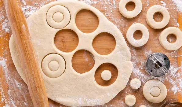 in the kitchen with stefano faita all purpose donut dough uncooked on a wooden board with portions cut out with a cookie cutter and rolling pin 